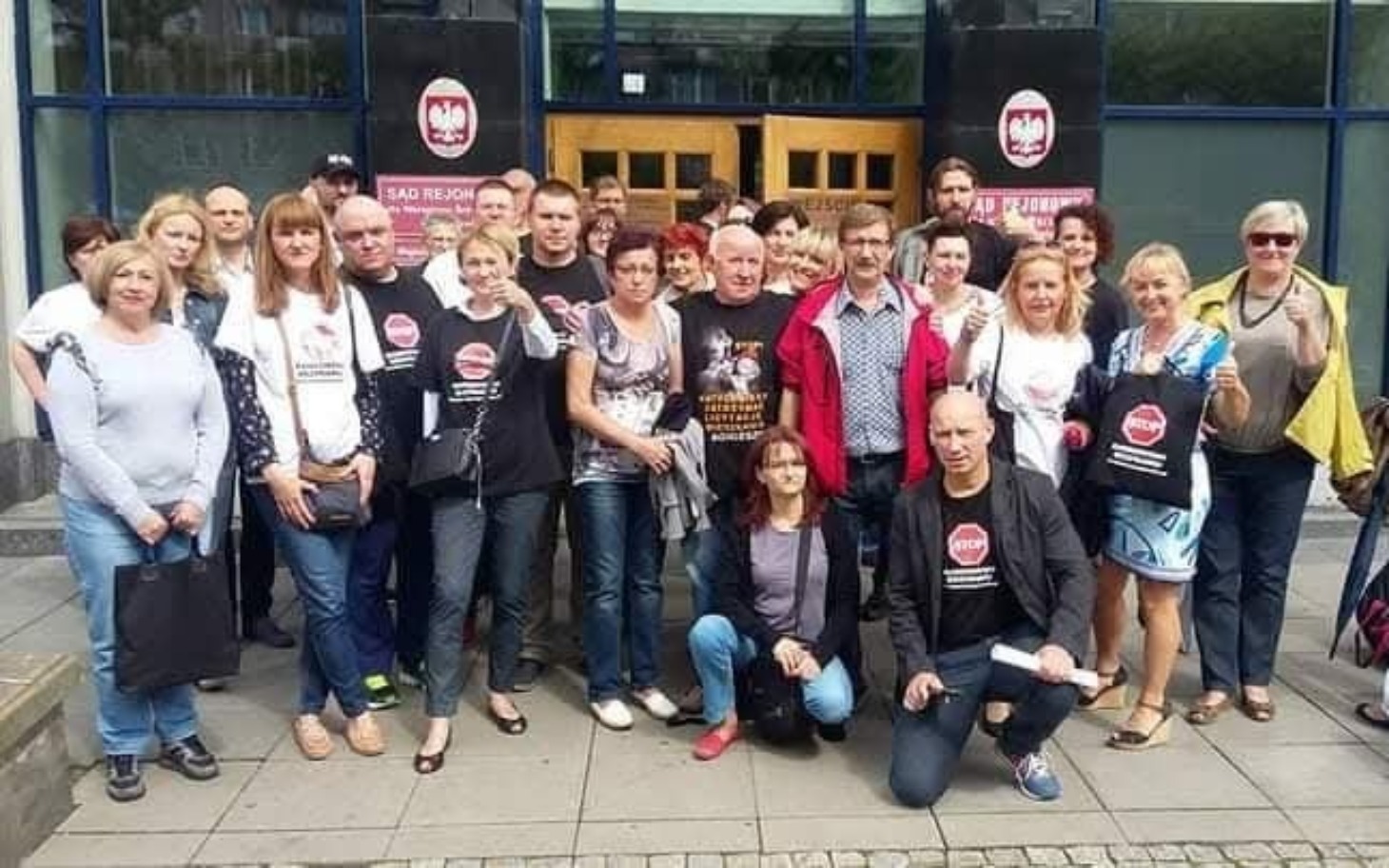 
        Grupa ludzi przed budynkiem, trzymających torby.
    