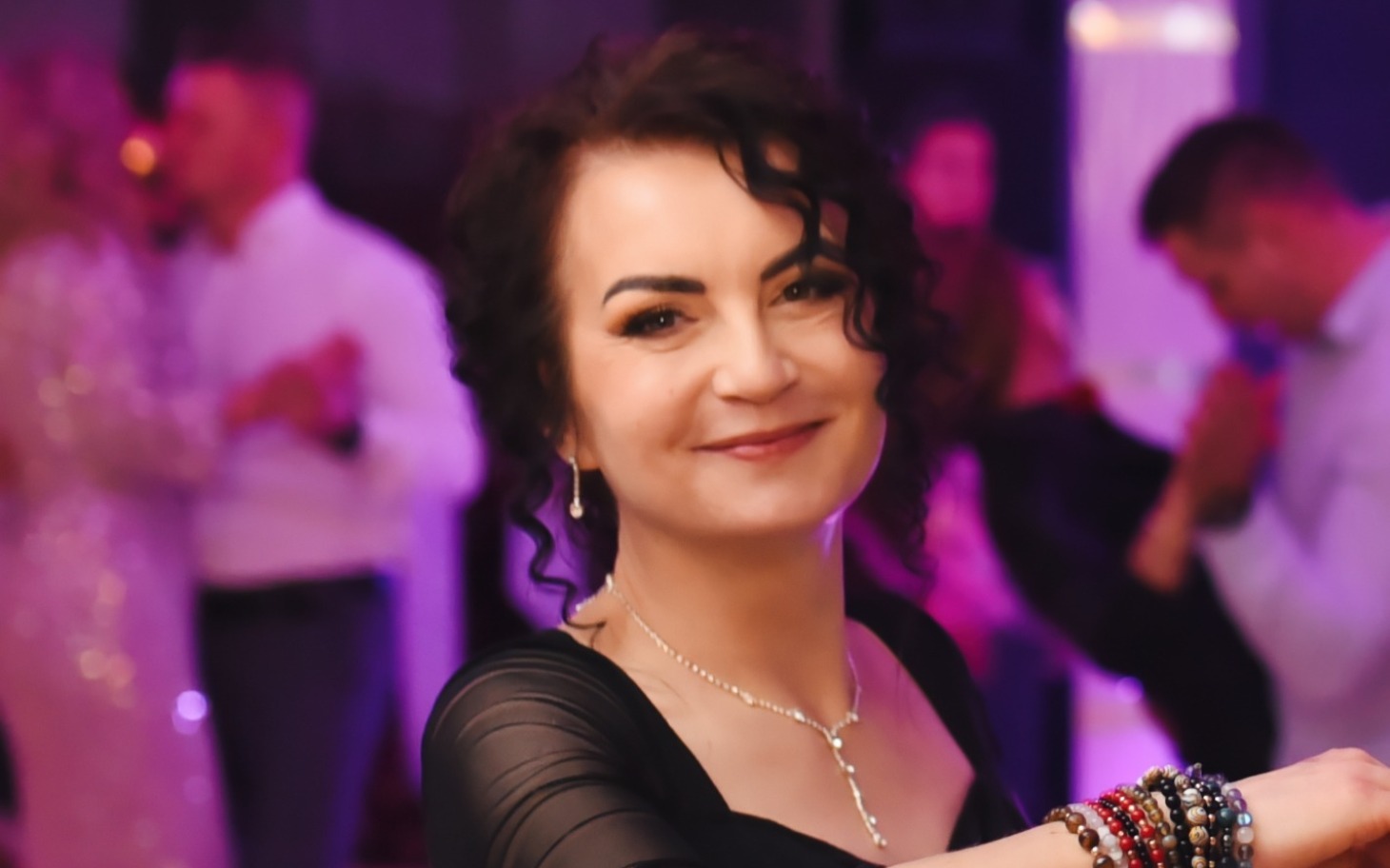 
        Kobieta w czarnej sukience, uśmiechająca się na imprezie.
    
