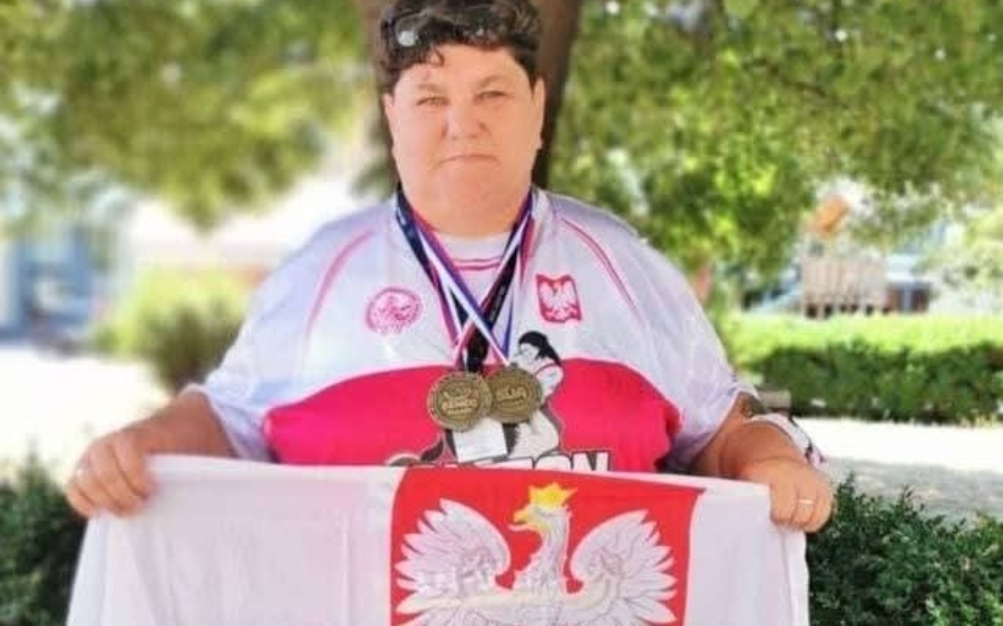 
        Kobieta z medalami i flagą Polski, duma z osiągnięć sportowych.
    