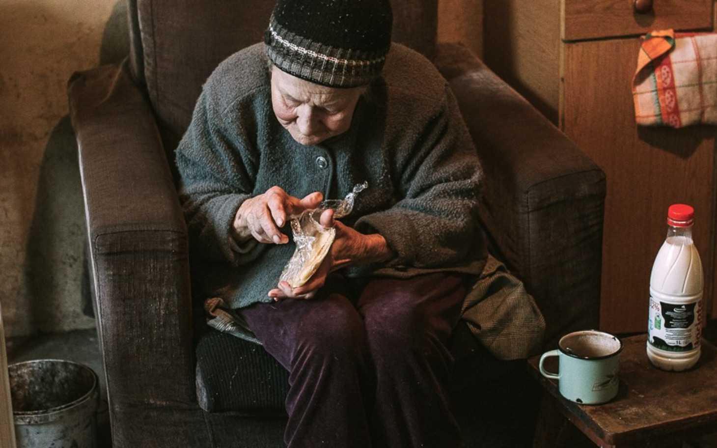 
        Starsza kobieta siedzi na fotelu, zajęta robieniem czegoś ręcznie.
    