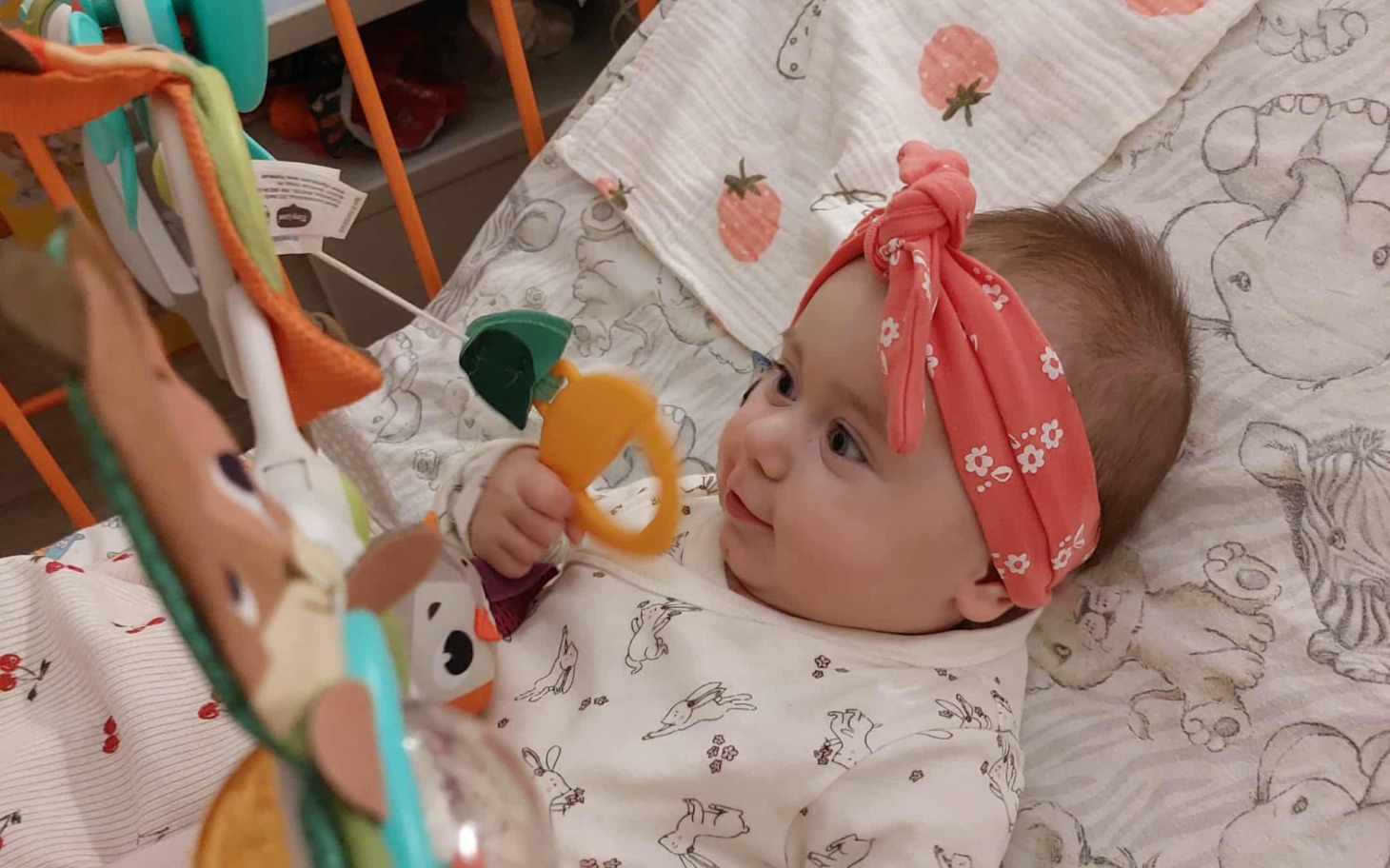 
        Mała dziewczynka bawi się zabawką w łóżeczku.
    