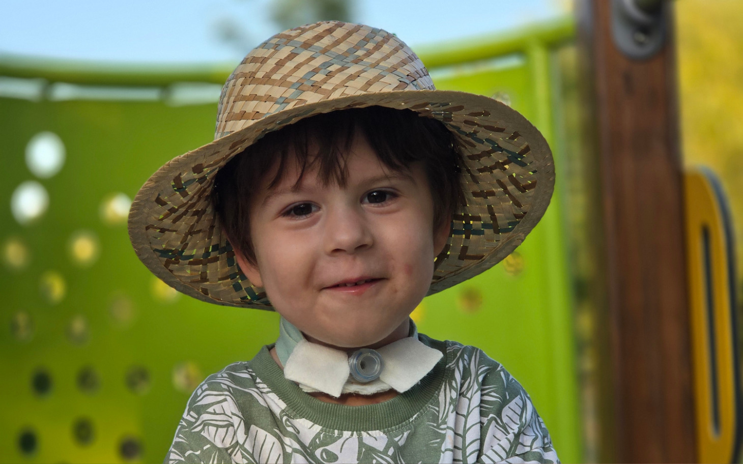 
        Chłopiec w kapeluszu, uśmiechający się na placu zabaw.
    