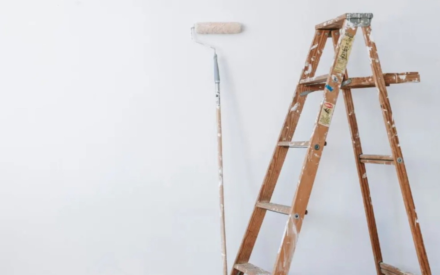 
        Drabina i wałek malarski na białej ścianie.
    