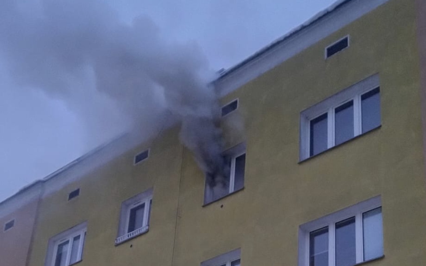 
        Dym wydobywający się z okna budynku, sygnalizujący pożar.
    