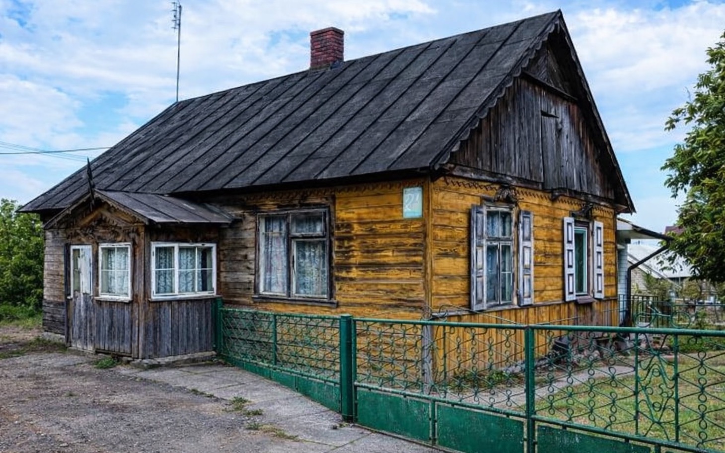 Stary drewniany dom z zielonym płotem, w słoneczny dzień.