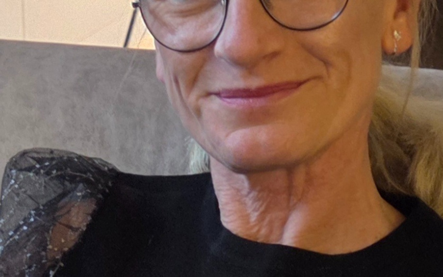 
        Uśmiechnięta kobieta w okularach, siedząca na kanapie.
    