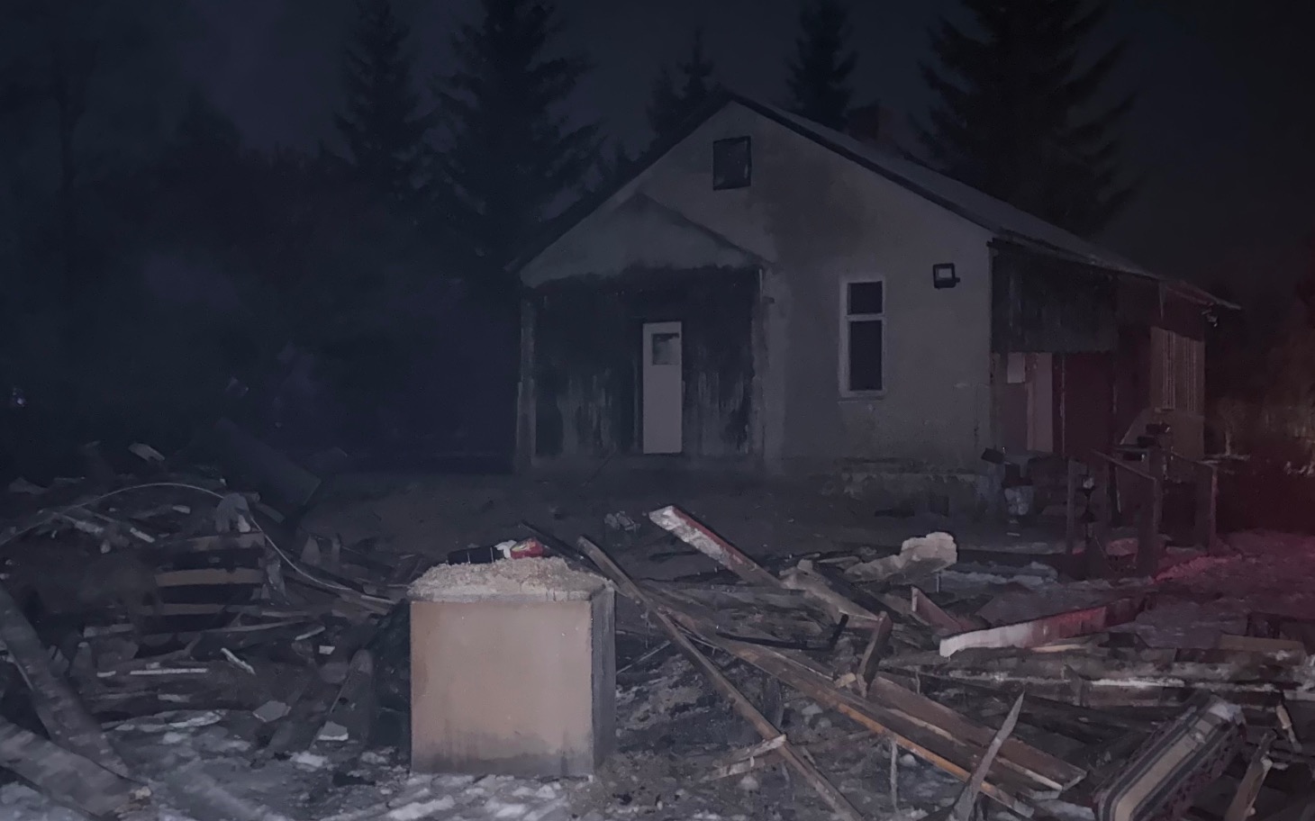 
        Zniszczony dom w nocy, otoczenie wygląda na opustoszałe.
    