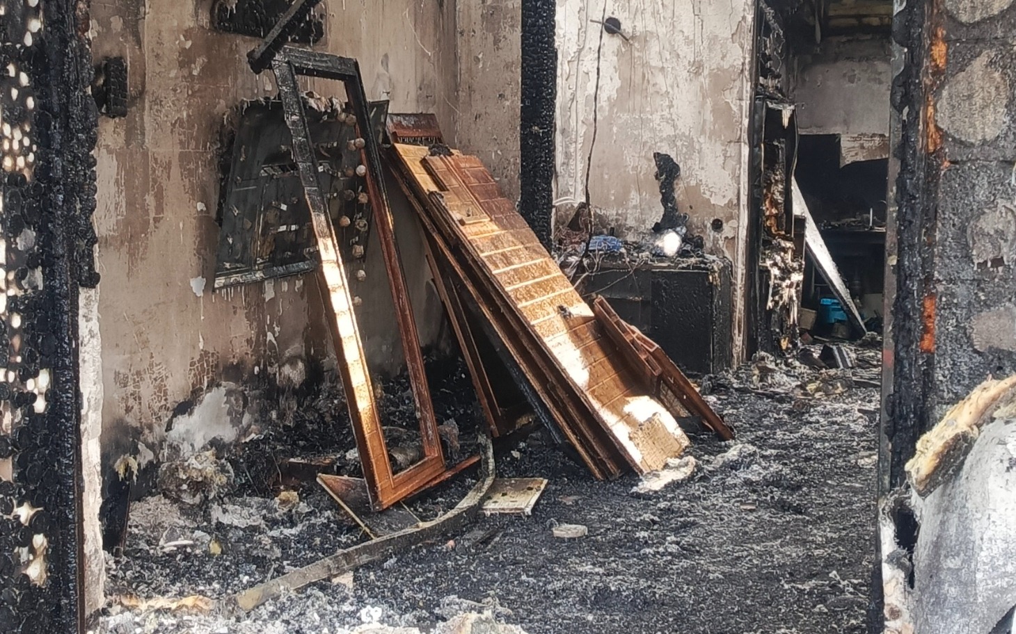 
        Zniszczony pokój po pożarze, z popalonymi meblami.
    