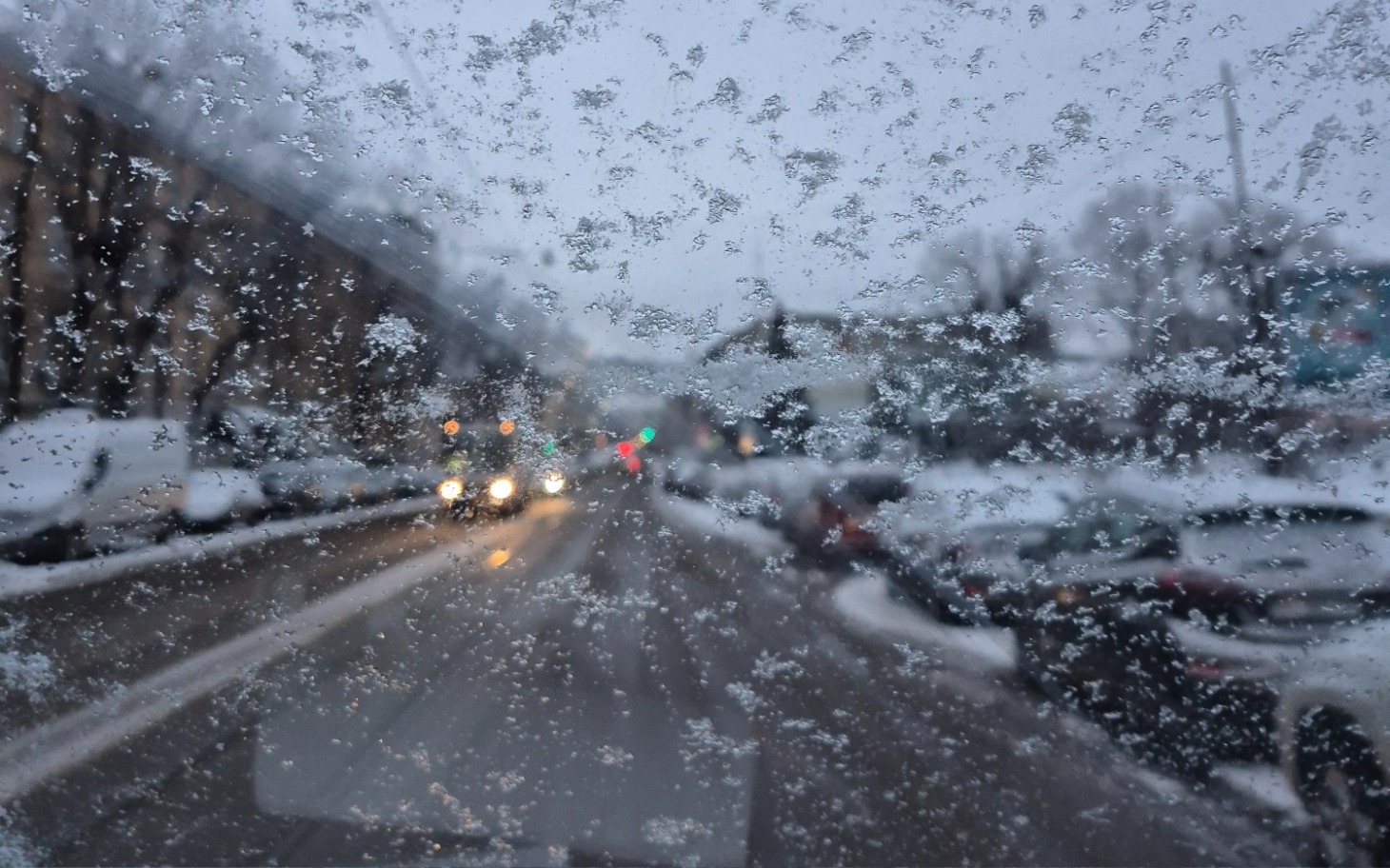 Zimowy widok na ulicę przez zaśnieżoną szybę samochodu.