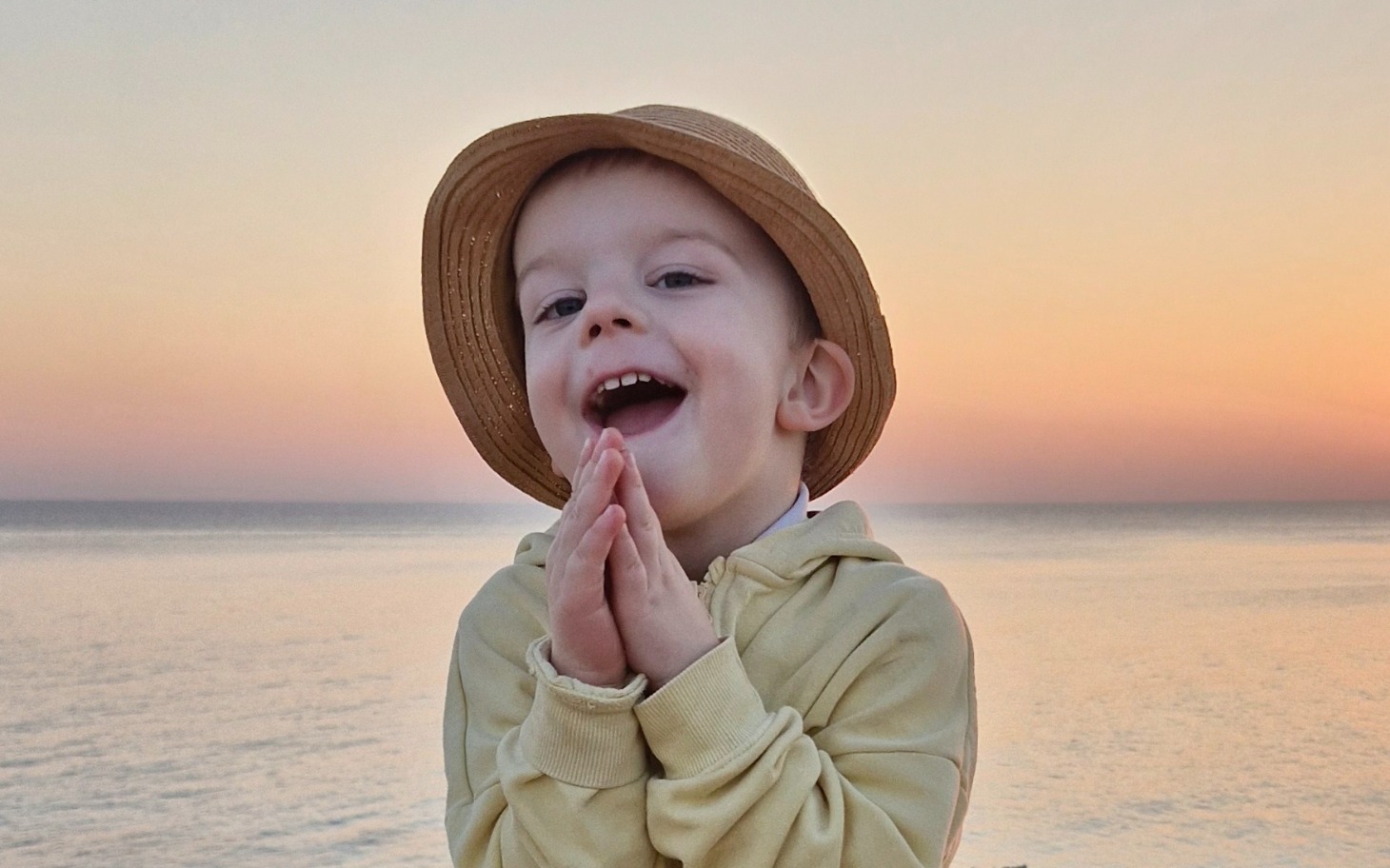 Chłopiec w kapeluszu, uśmiechający się na tle morza.