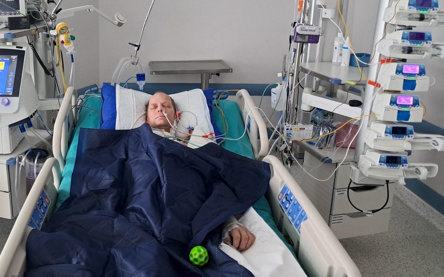 
        Mężczyzna leżący w szpitalnym łóżku z aparaturą.
    