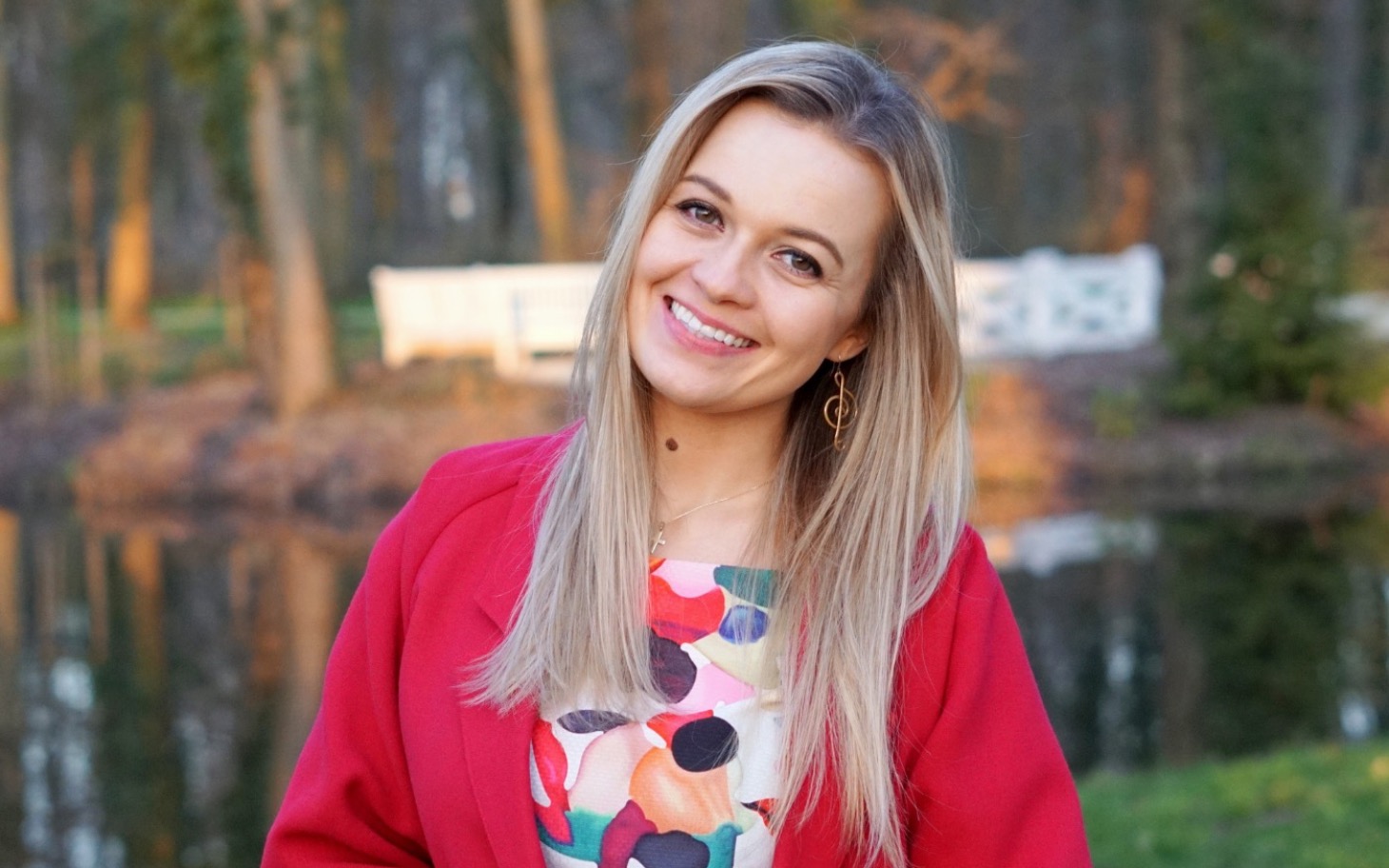 
        Uśmiechnięta kobieta w kolorowej sukience na tle przyrody.
    