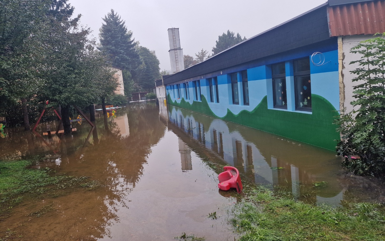 
        Widok na zalany teren wokół budynku, z zabawką na podwórku.
    