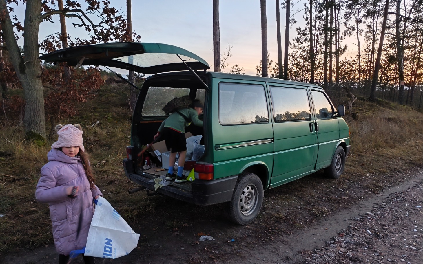 
        Dzieci pomagają przy pakowaniu rzeczy do zielonego vana w lesie.
    