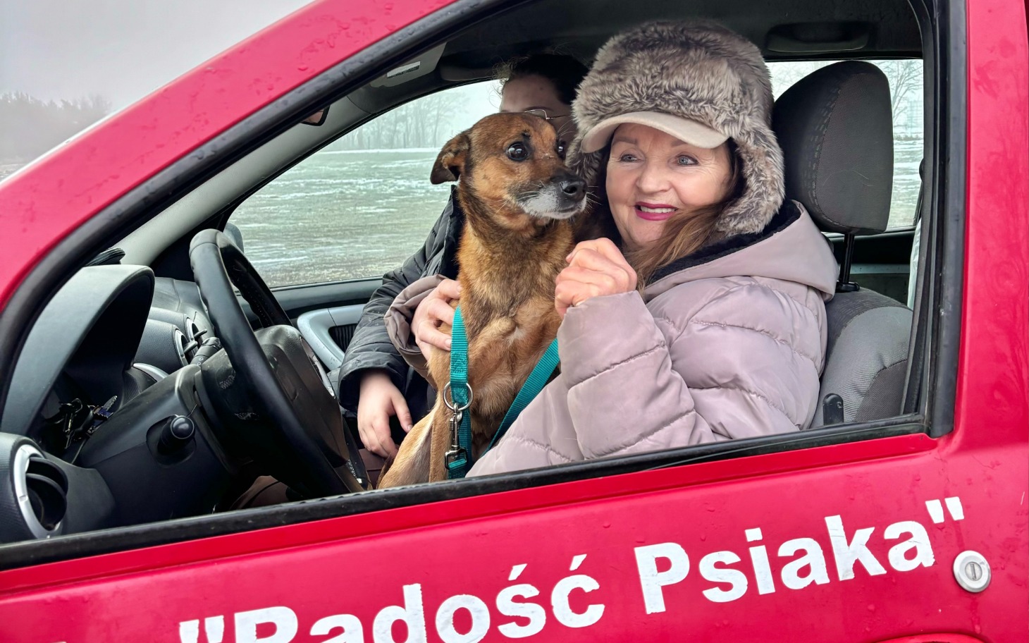 
        Kobieta w samochodzie z psem na rękach.
    