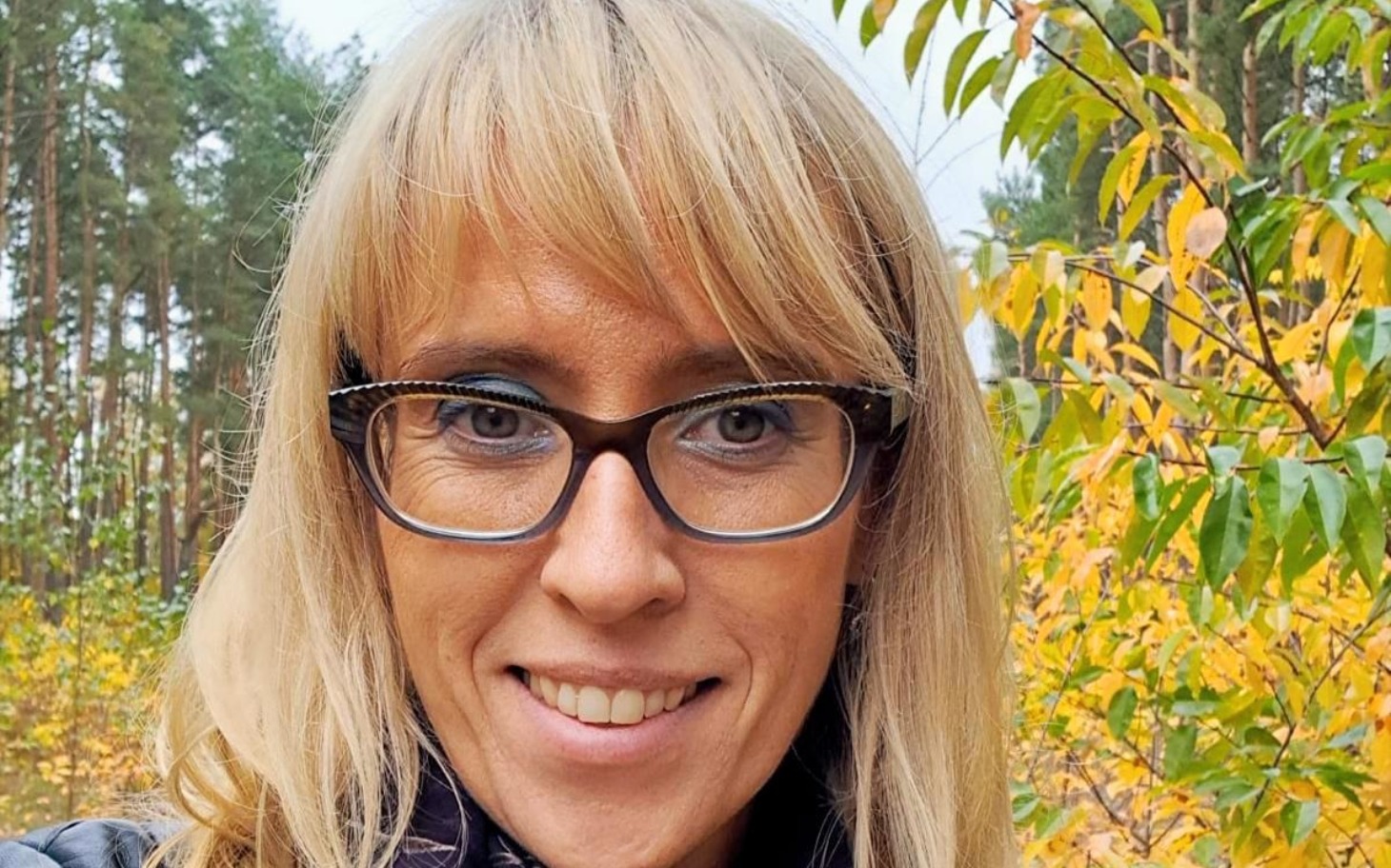 
        Kobieta w okularach na tle jesiennego lasu.
    