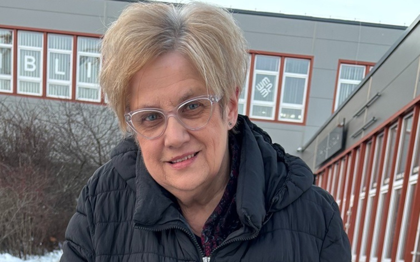 
        Kobieta w okularach, uśmiechająca się na tle budynku.
    