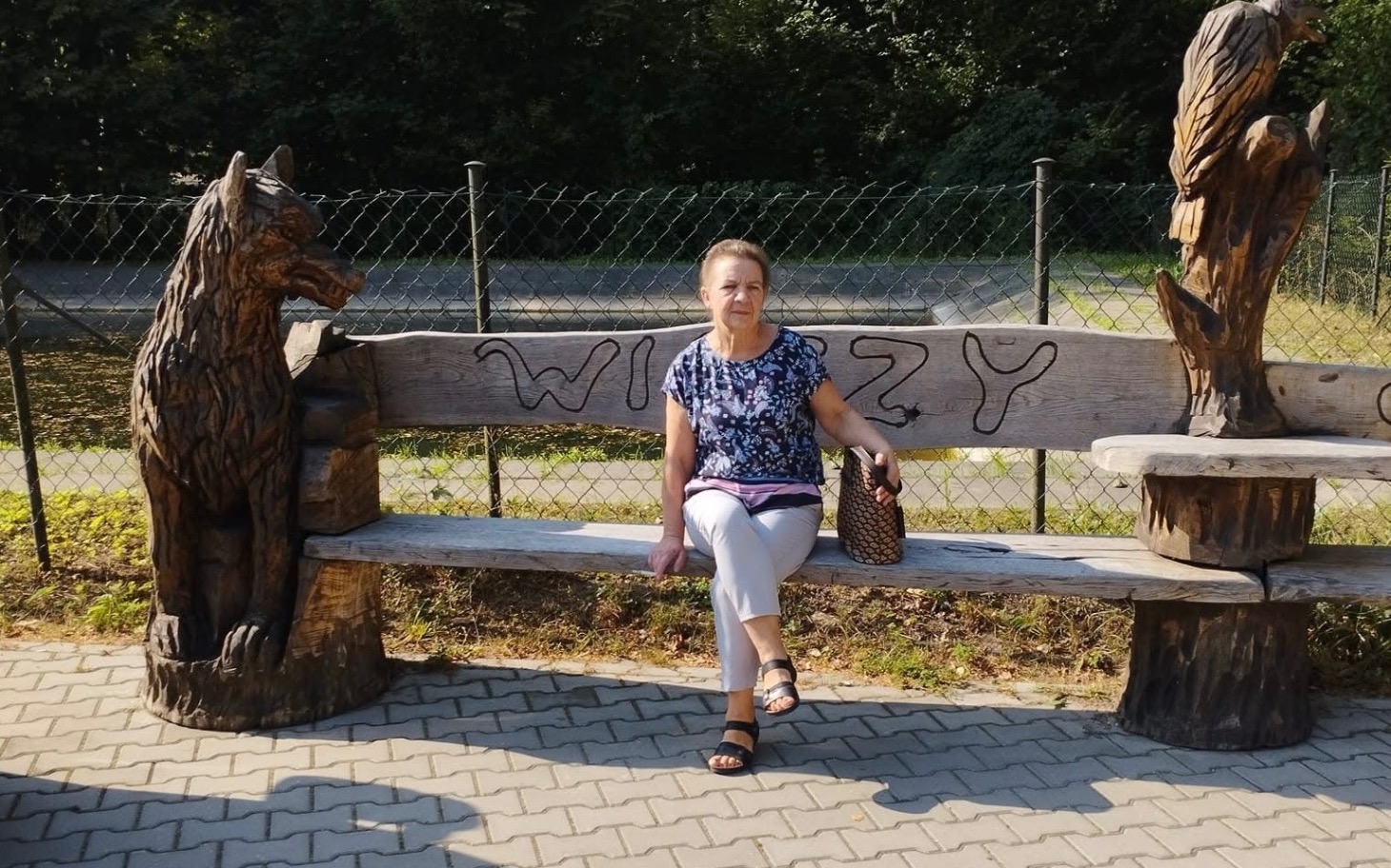 
        Kobieta siedząca na rzeźbionej ławce w parku.
    