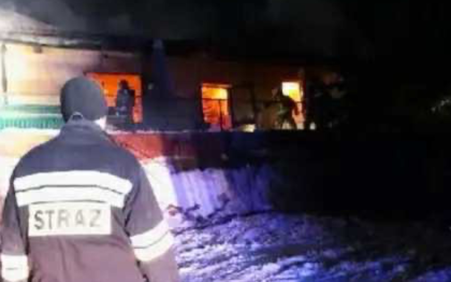 
        Strażak obserwujący pożar w budynku nocą.
    