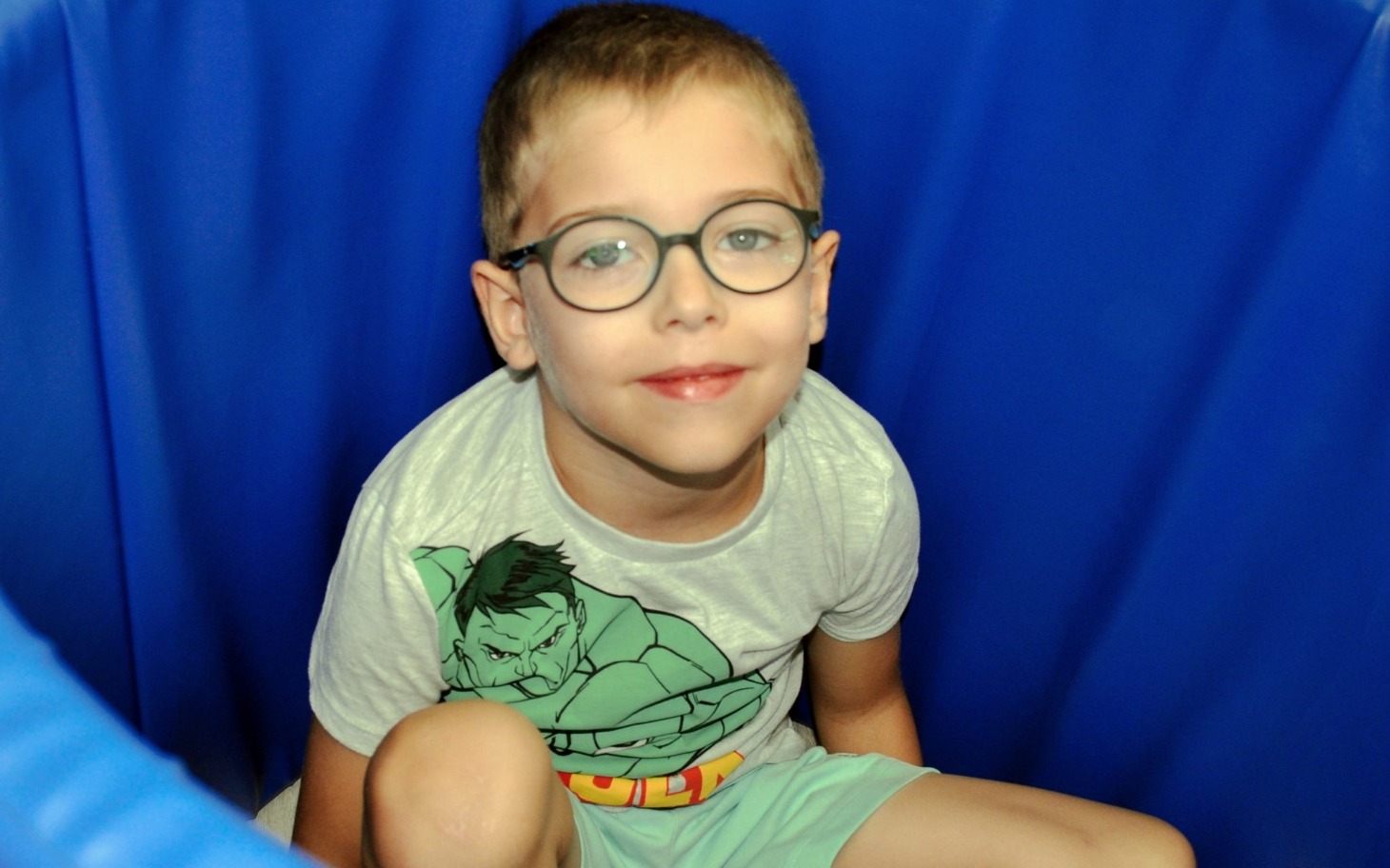 
        Chłopiec w okularach siedzi w niebieskim pojemniku.
    