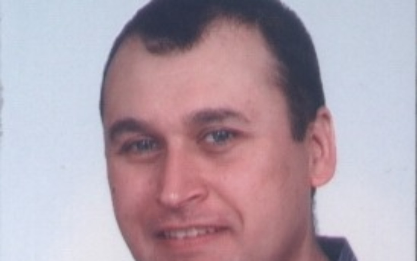 
        Mężczyzna na zdjęciu paszportowym z uśmiechem.
    