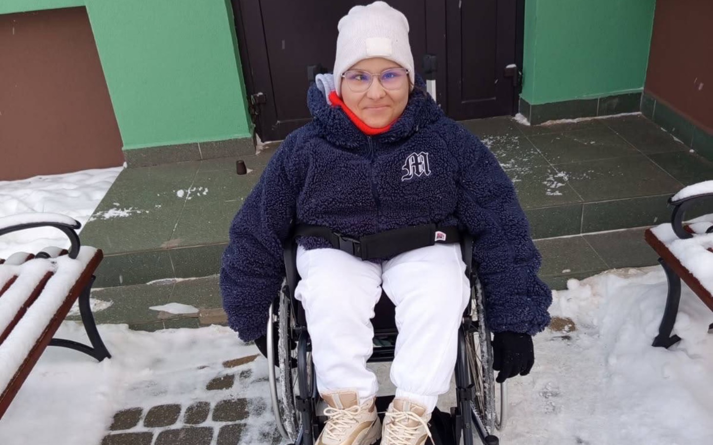
        Młoda dziewczyna w wózku inwalidzkim na tle zielonej ściany.
    