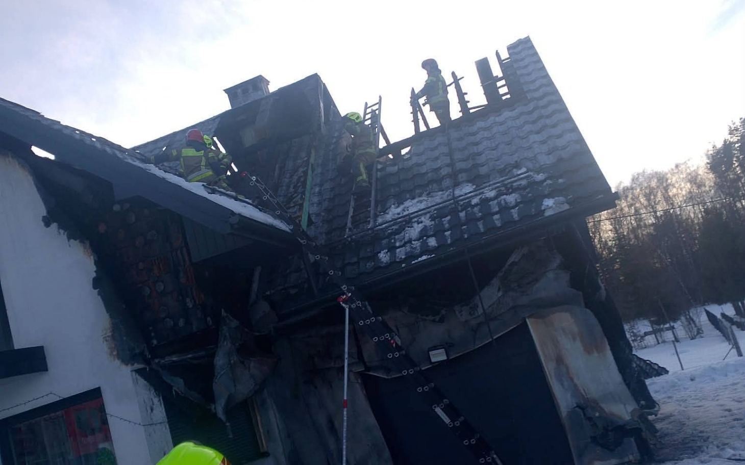 
        Strażacy pracujący na dachu zniszczonego budynku po pożarze.
    