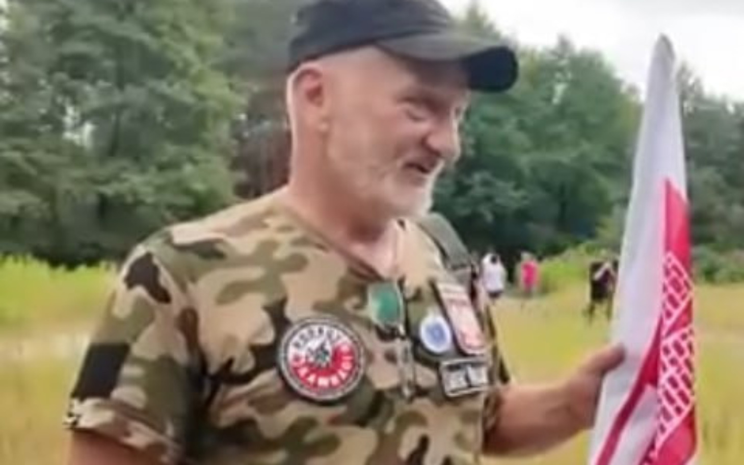 
        Mężczyzna w kamuflażu trzymający flagę w lesie.
    