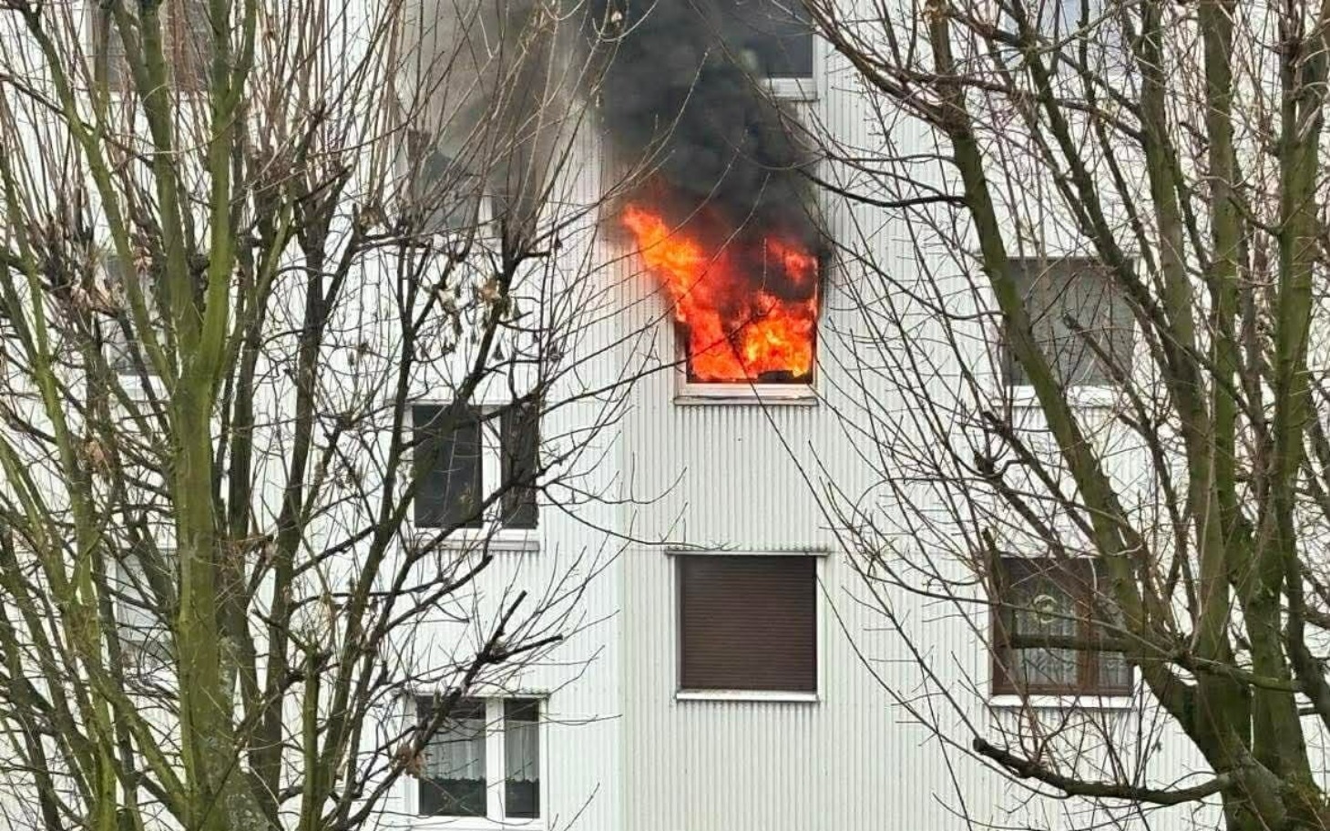 
        Pożar w oknie budynku, dym i płomienie.
    