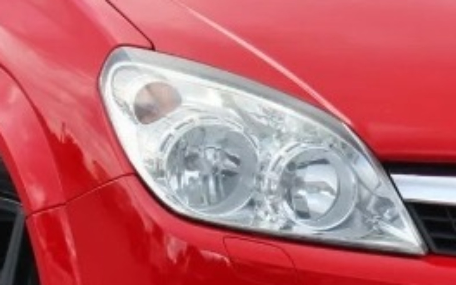 
        Zbliżenie na reflektor czerwonego samochodu.
    