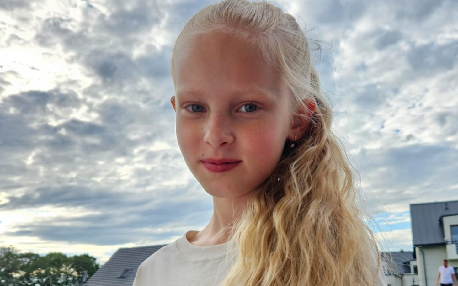 
        Portret dziewczynki z długimi włosami na tle chmur.
    