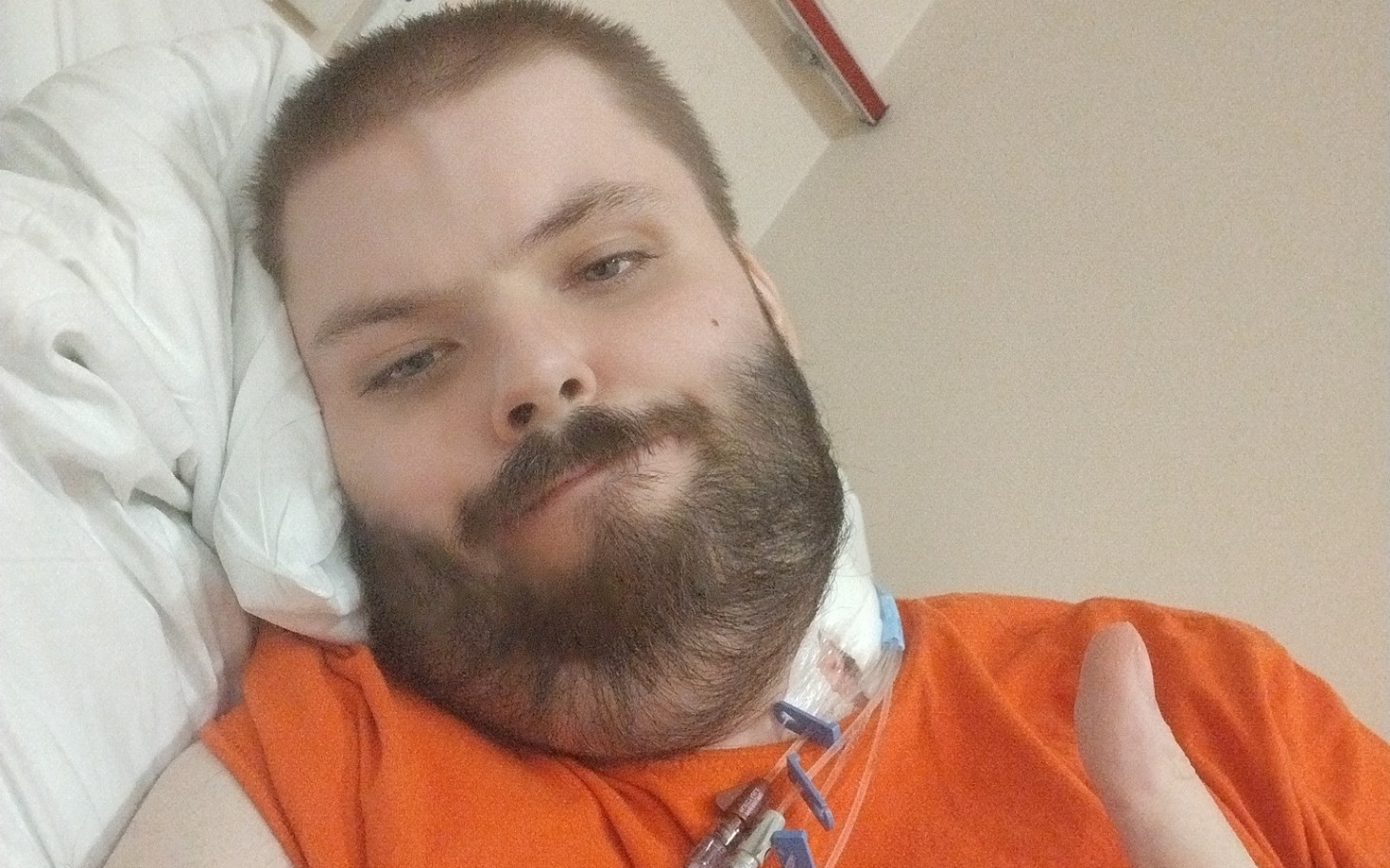 
        Mężczyzna w szpitalu, leżący na łóżku, pokazujący kciuk w górę.
    