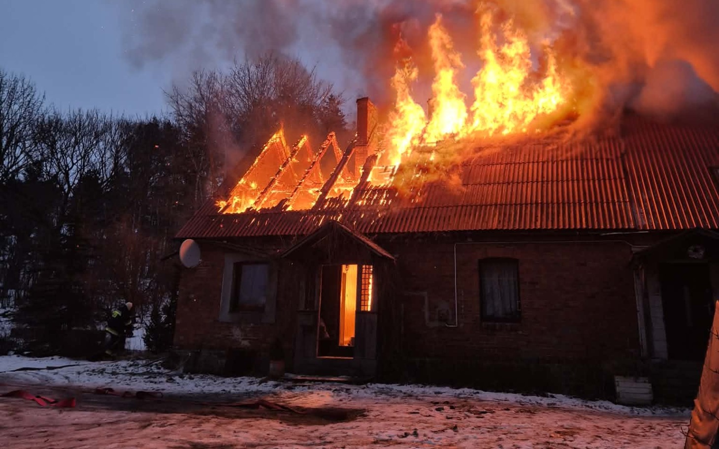 
        Pożar na dachu domu, ogień i dym w zimowej scenerii.
    