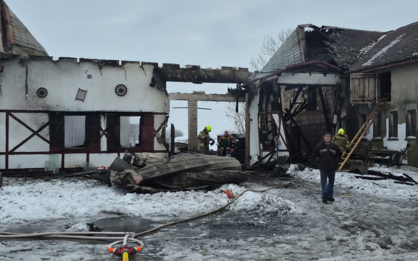 
        Zniszczony budynek po pożarze, w tle strażacy.
    