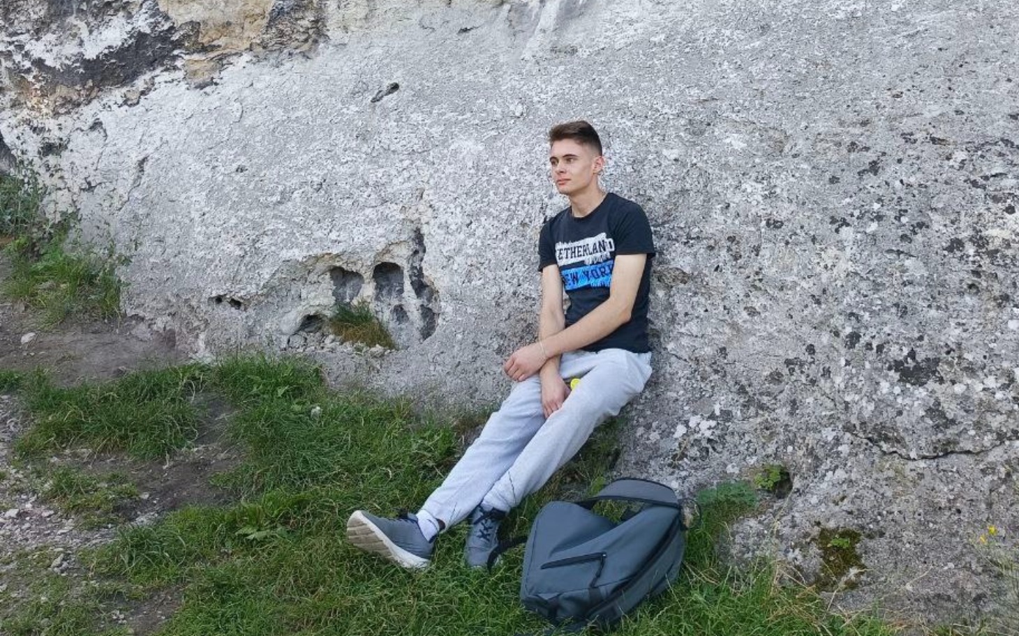 
        Młody mężczyzna siedzący na tle skalnej ściany.
    