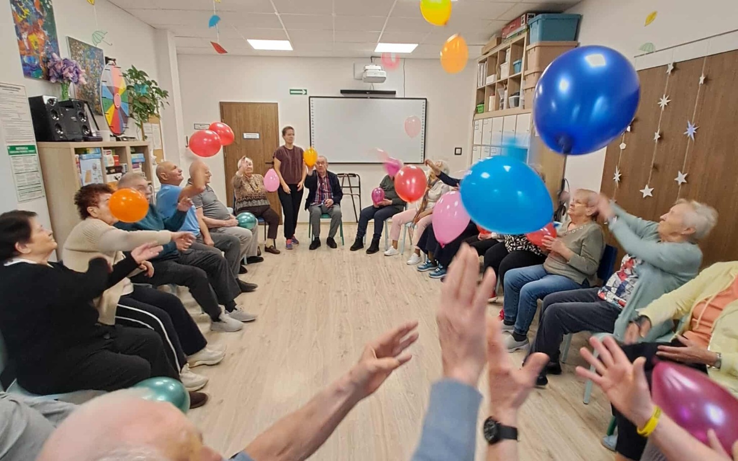 Seniorzy bawią się balonami w radosnej atmosferze.