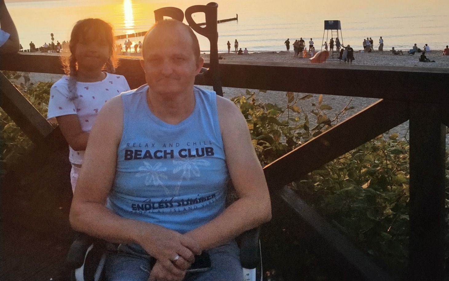 
        Starszy mężczyzna z córką na tle plaży podczas zachodu słońca.
    