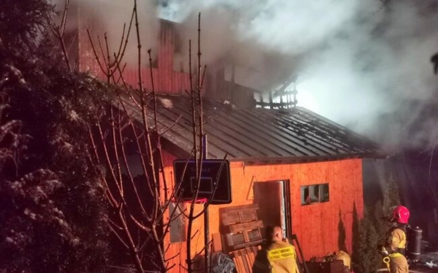 
        Pożar w drewnianym budynku, dym unosi się w powietrzu.
    