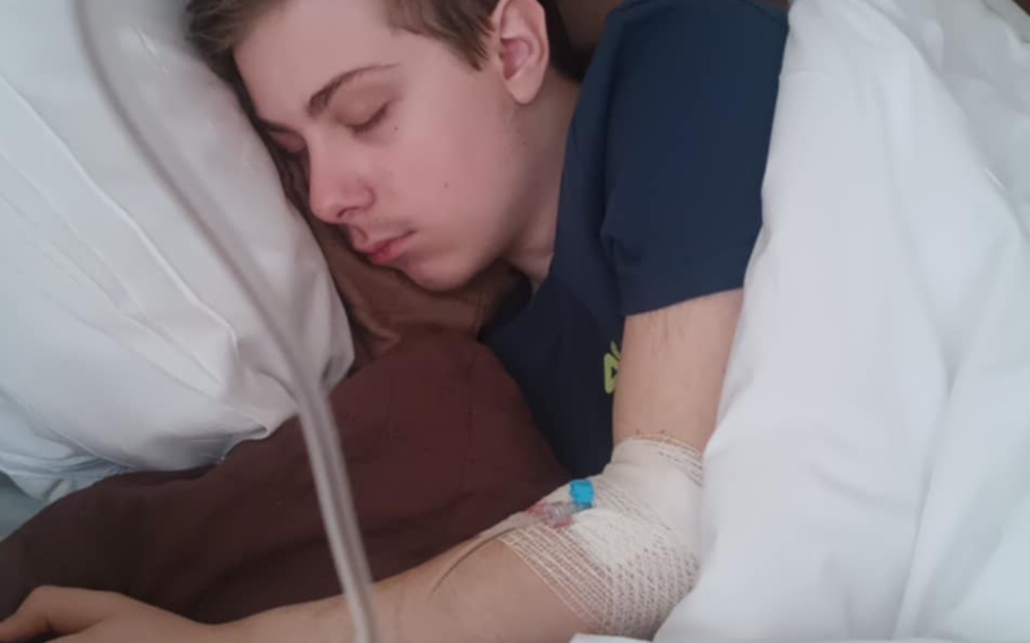 
        Chłopak śpiący w łóżku z opatrunkiem na ręce.
    