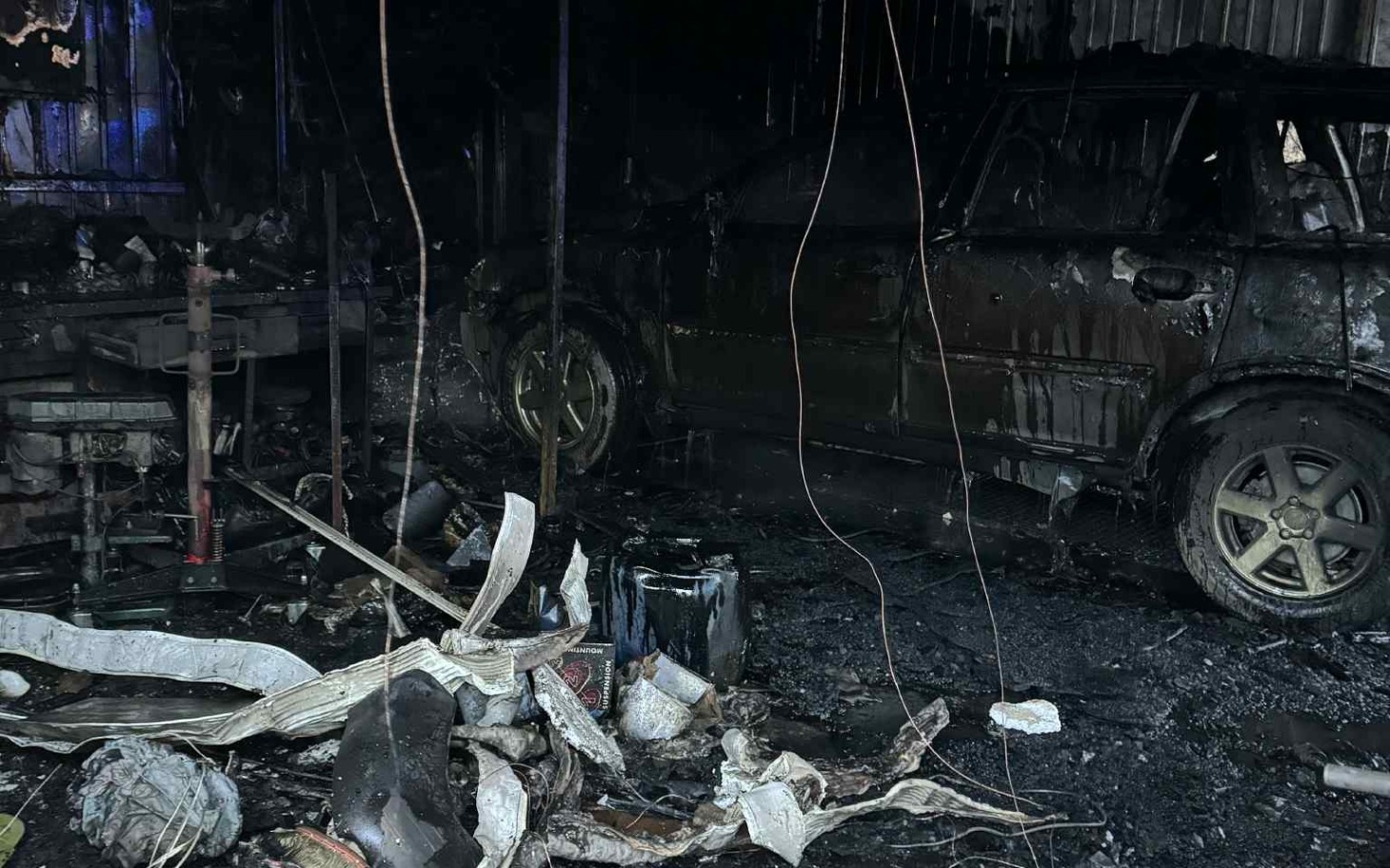 
        Zniszczony warsztat z wrakiem samochodu po pożarze.
    