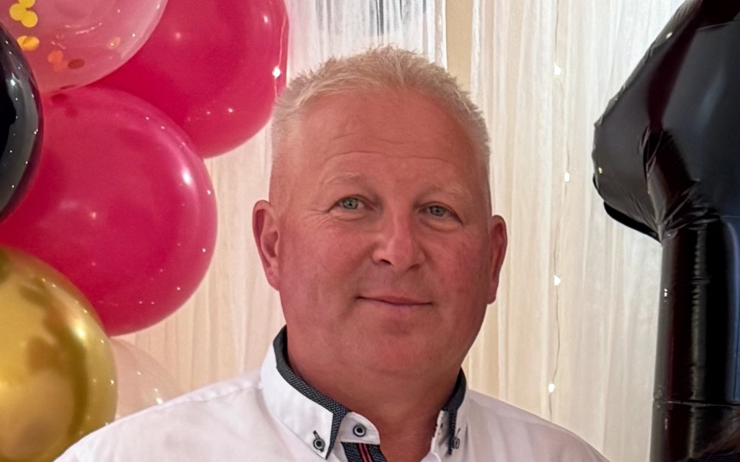 
        Mężczyzna uśmiechający się na tle kolorowych balonów.
    