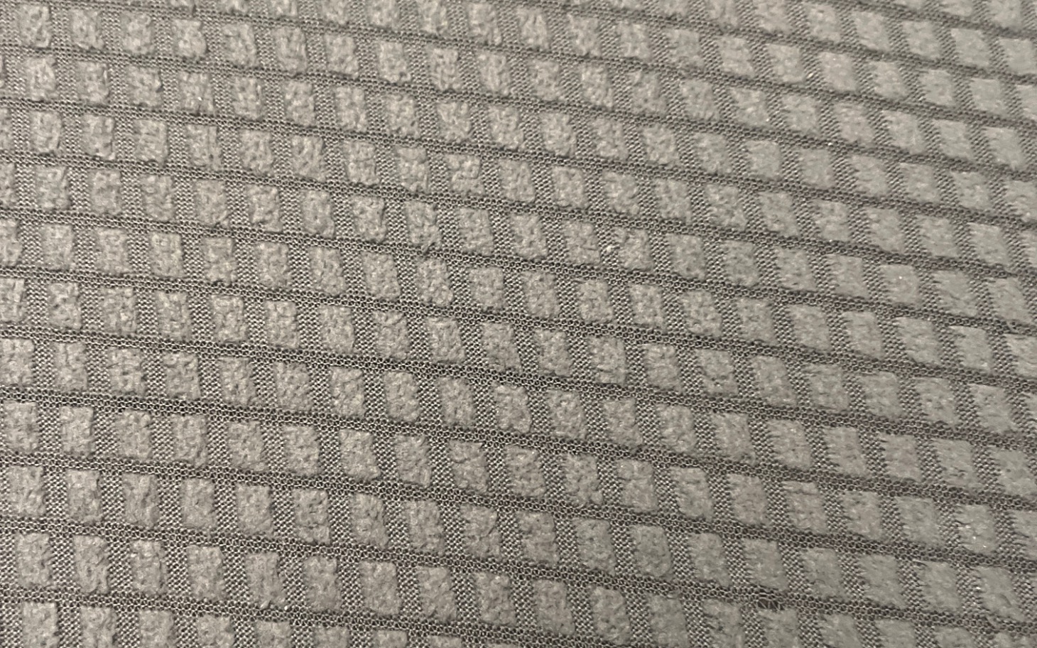 
        Zbliżenie na szary materiał z wyraźnym wzorem.
    