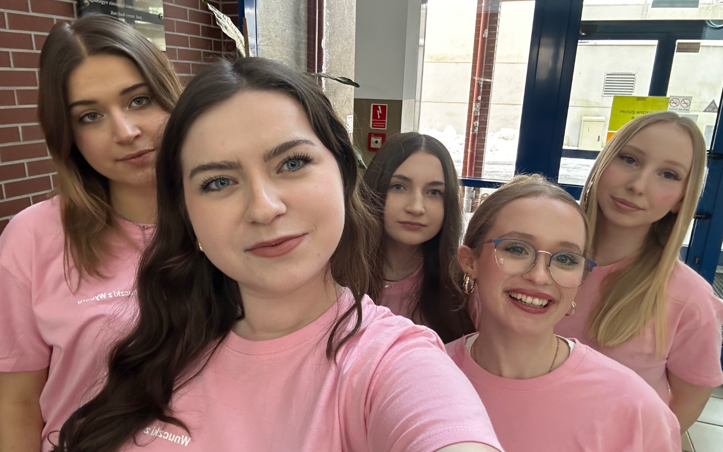 
        Grupa pięciu dziewczyn w różowych koszulkach, selfie.
    