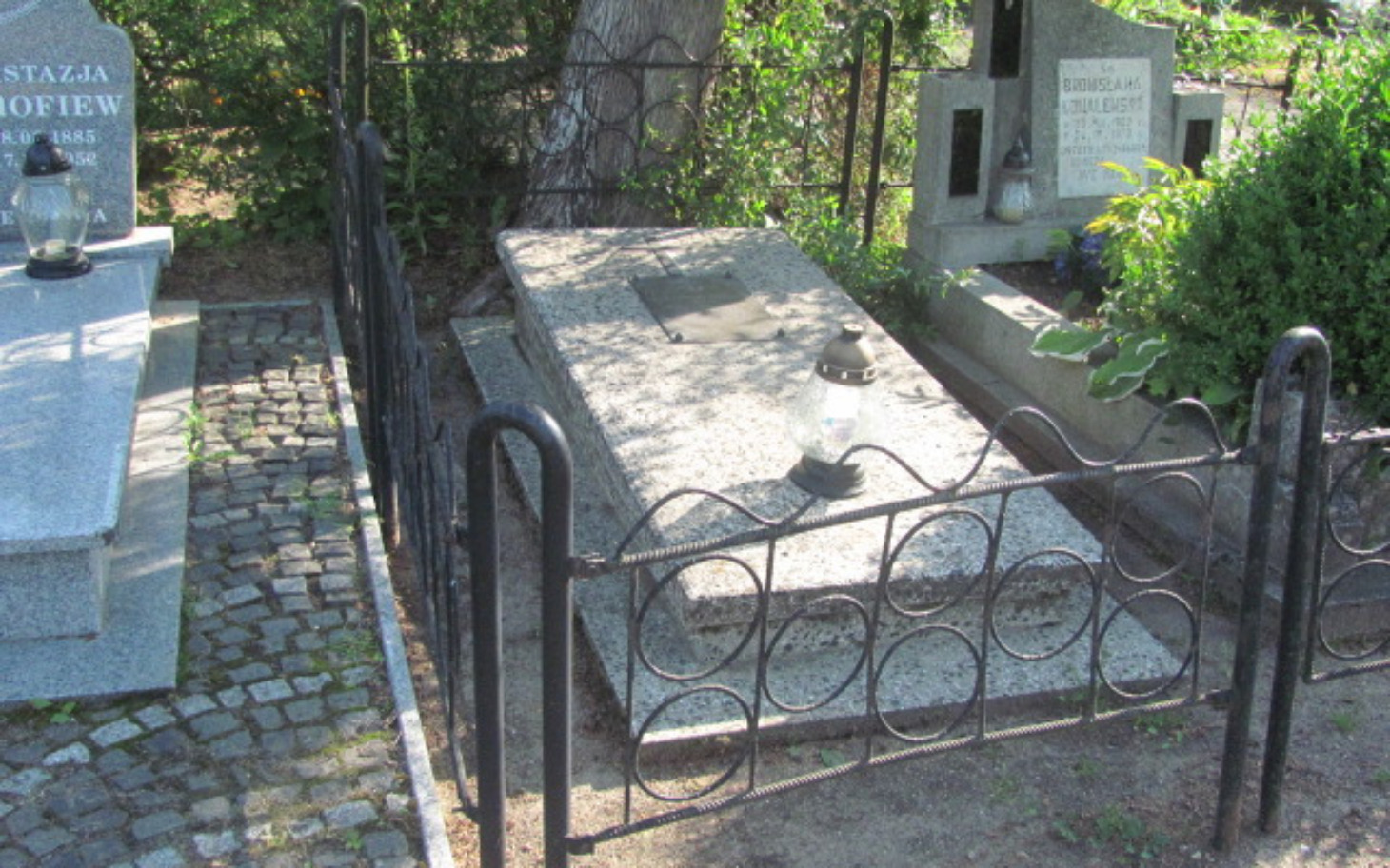 
        Grób z lampionem na cmentarzu, otoczony metalowym ogrodzeniem.
    