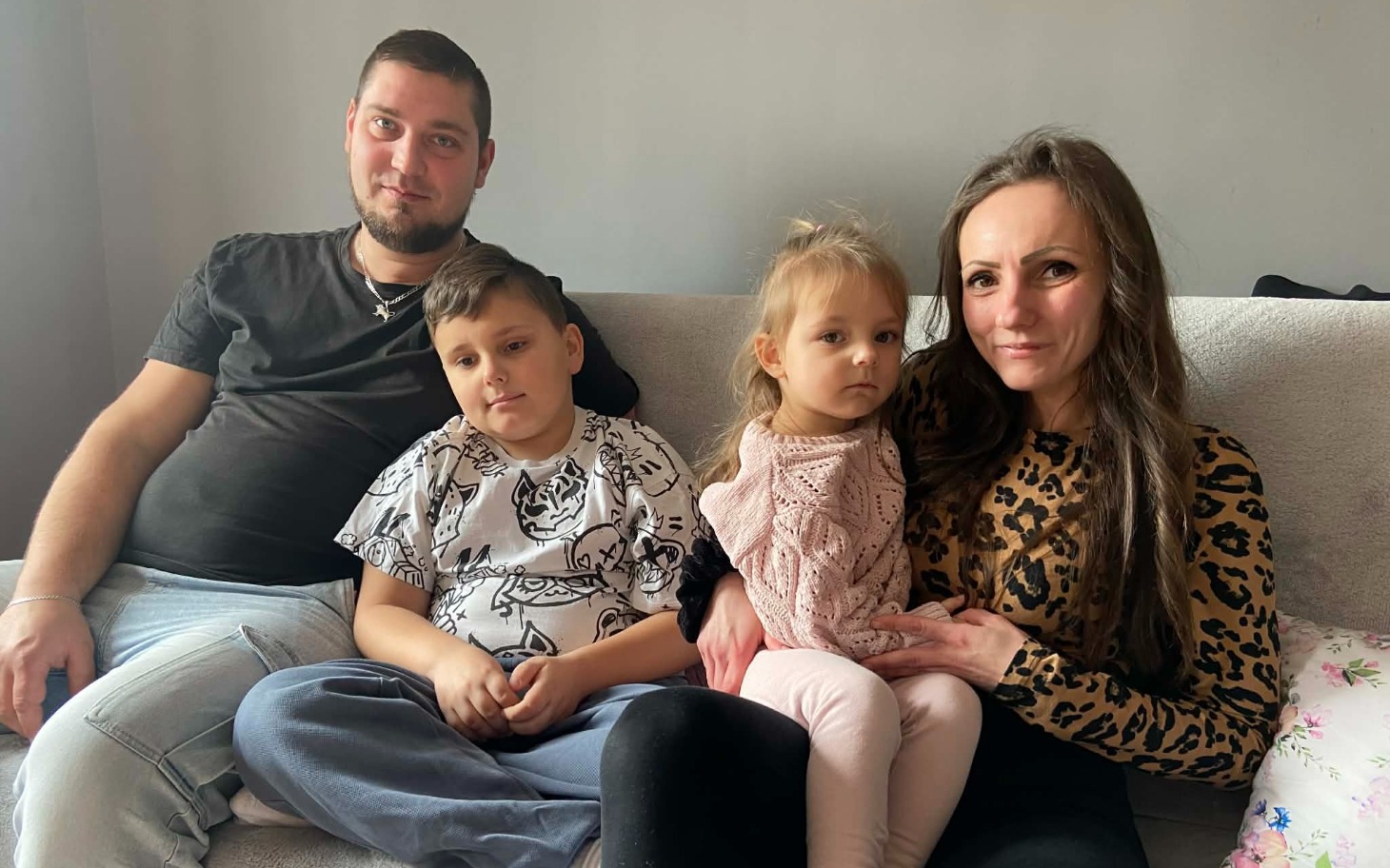 
        Rodzina siedząca na kanapie, uśmiechająca się do kamery.
    