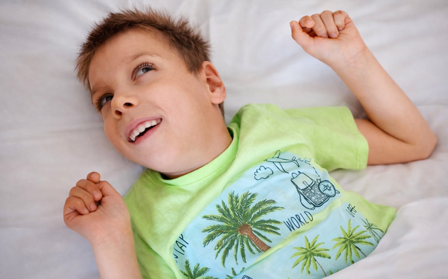 
        Chłopiec leży w łóżku, uśmiecha się i wygląda radośnie.
    