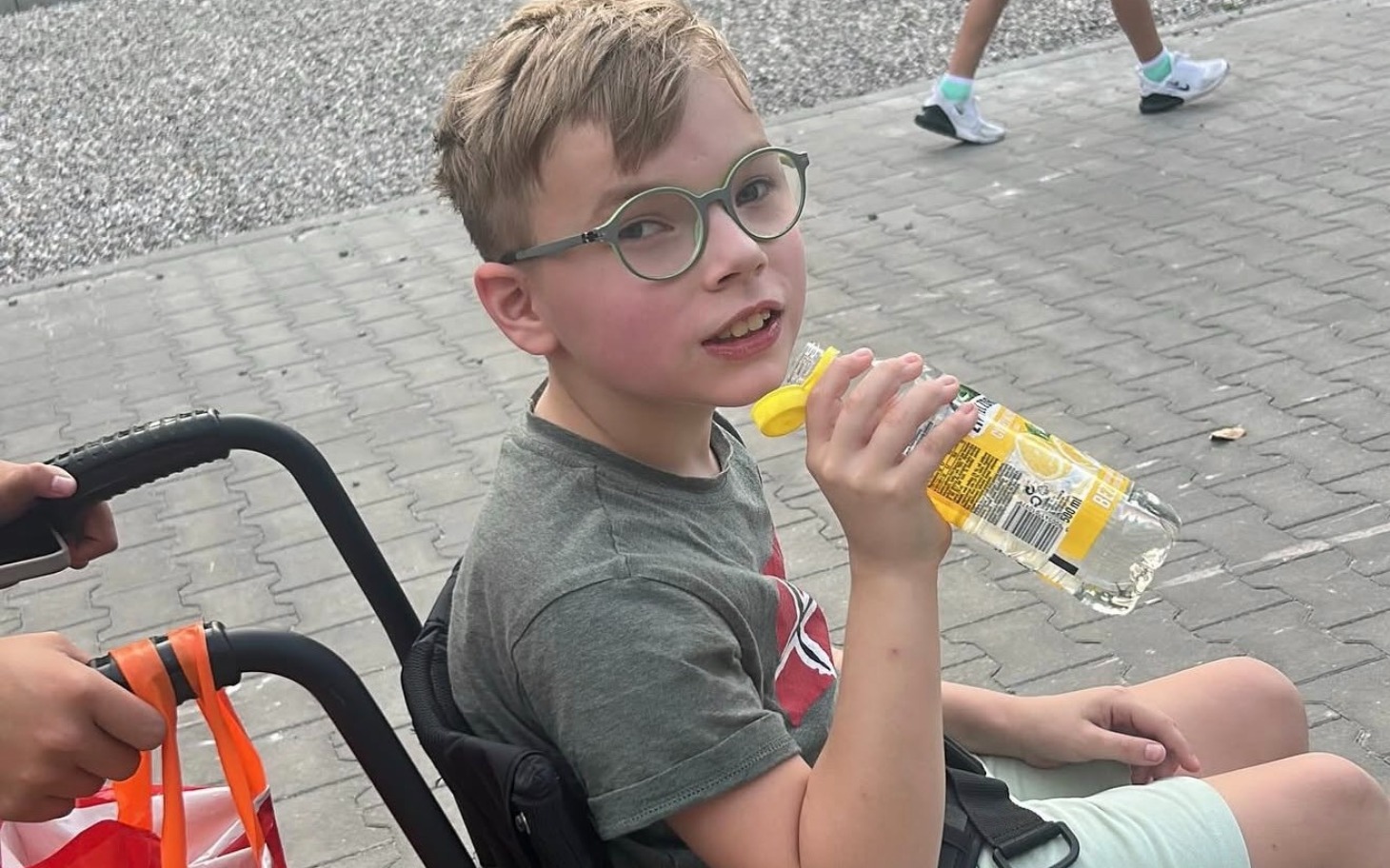 
        Chłopiec w wózku, pijący napój w parku.
    