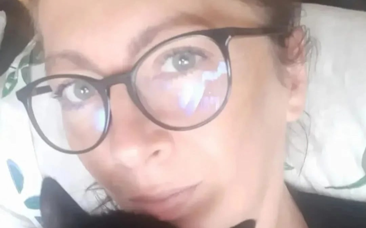 
        Kobieta z okularami trzyma kota na ramieniu, uśmiechając się do kamery.
    