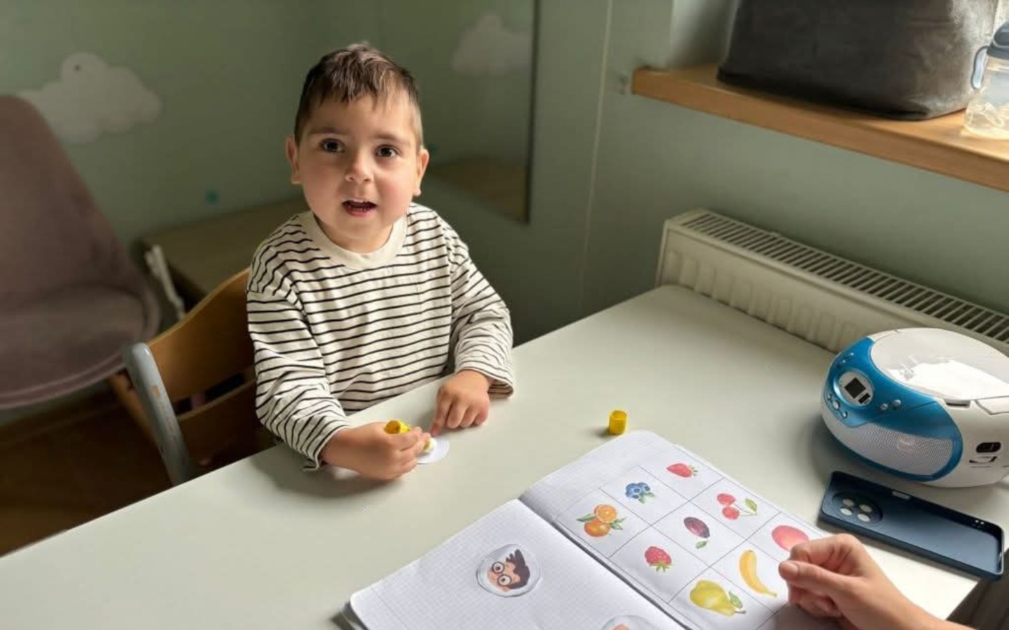 
        Chłopiec bawi się przy stole, używając kolorowych naklejek.
    