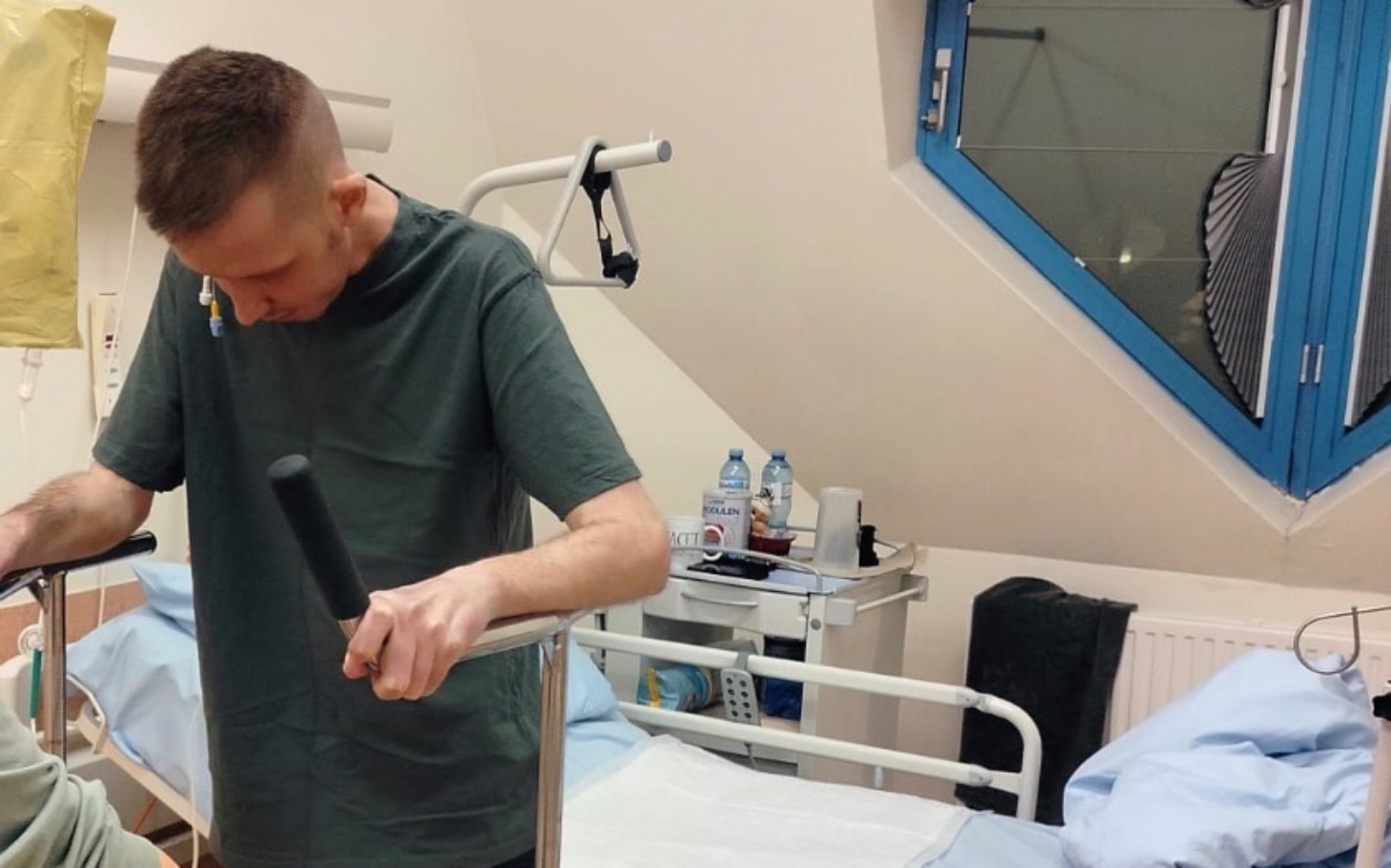 
        Mężczyzna w szpitalu, trzymający się poręczy łóżka.
    